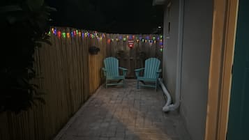 A patio area with two chairs and a wooden fence, decorated with colorful lights.