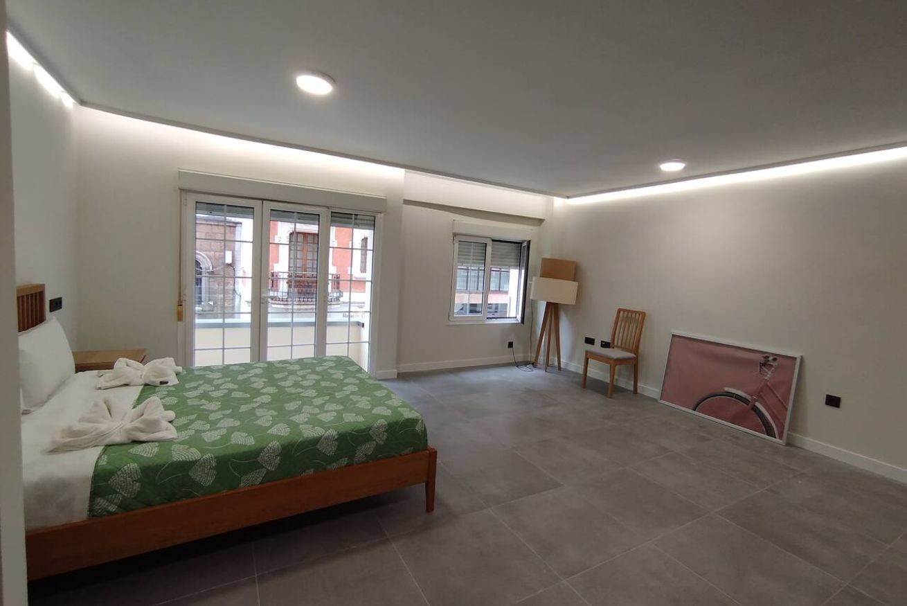 Un dormitorio con cama, una silla, una lámpara y un ventanal grande.