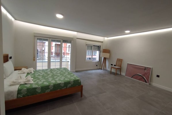 Een slaapkamer met een bed, een stoel, een lamp en een groot raam.