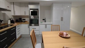 A modern kitchen with white cabinets, a built-in oven, and a dining table with a tray of food.