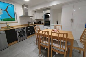 Een kleine keuken met een wasmachine, een eettafel met stoelen en een grote kast.