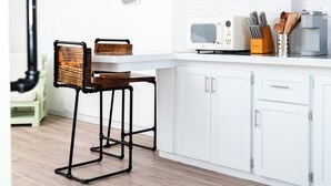 A modern kitchen with white cabinets, a wooden floor, and a dining area with a chair and table. - The Barnyard is a chic, cozy open concept studio apartment.  (Sion Hill)