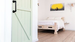 A room with a green door, a bed with white bedding, a wooden floor, and a painting of a yellow tree on the wall. - The Barnyard is a chic, cozy open concept studio apartment.  (Sion Hill)