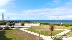 Área da piscina com vista para o mar, uma estrutura alta ao fundo e céu limpo.
