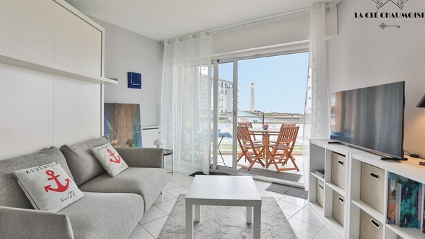 Uma sala de estar moderna com sofá, mesa de centro, televisão e uma varanda com mesa e cadeiras.