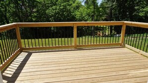 A wooden deck with a railing, surrounded by a grassy area and trees. - Family-friendly home, dedicated workspace, minutes from Cincinnati attractions! (Cincinnati)