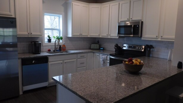 A modern kitchen with white cabinets, a granite countertop, stainless steel appliances, and a window providing natural light. - Family-friendly home, dedicated workspace, minutes from Cincinnati attractions! (Cincinnati)