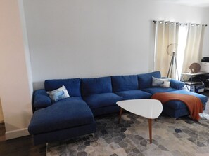 A living room with a blue sectional sofa, a white coffee table, and a floor with hexagonal tiles.