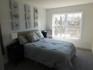 A bedroom with a bed, a nightstand, a dresser, and a window.