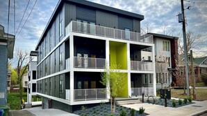 Un immeuble résidentiel moderne à plusieurs étages, doté de balcons, d’un mur d’accent vert et d’un jardin paysager à l’avant.