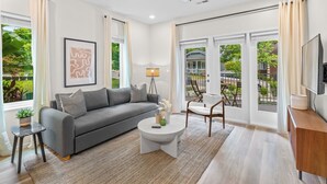 Un salon moderne avec un canapé gris, une table basse ronde et un téléviseur posé sur un meuble en bois.