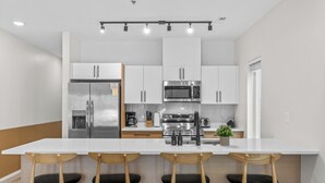 Une cuisine moderne avec des meubles blancs, des appareils en acier inoxydable et un îlot central doté de tabourets de bar.