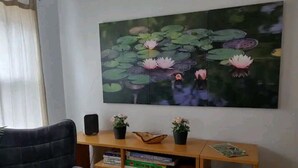 Ein Wohnzimmer mit einem großen Gemälde von Seerosen, einem schwarzen Ledersessel, einer Holzbibliothek mit Büchern und Dekorationen sowie einem weißen Mülleimer.