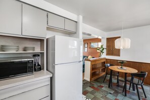Compact kitchen with modern appliances, microwave, blender, and refrigerator. Dining area with wooden table and two chairs.
