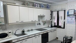 Une cuisine compacte avec des meubles blancs, un évier, un four à micro-ondes et un lave-vaisselle. Des assiettes décoratives sont accrochées au mur, au-dessus des meubles, et un calendrier est affiché sur le mur, à droite.