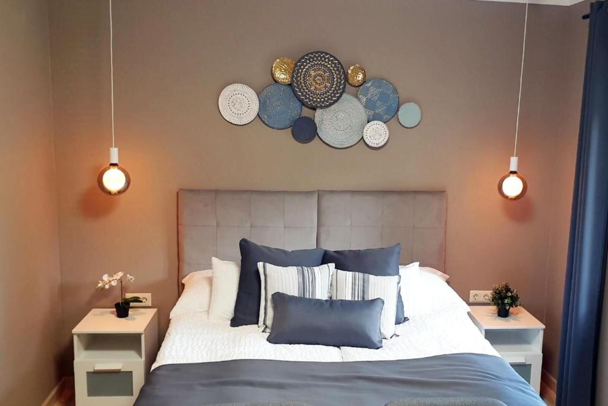 Un dormitorio ordenado con cama, almohadas, mesitas de noche y decoración en la pared.
