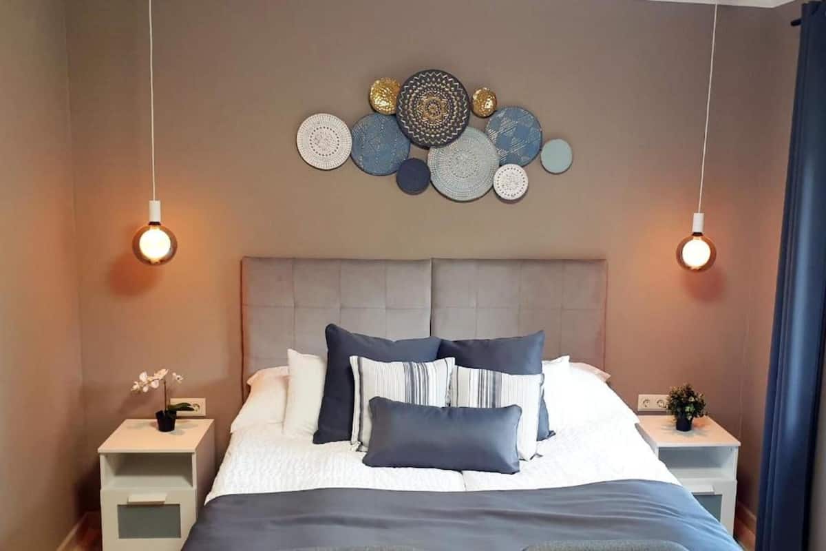 A neatly arranged bedroom with a bed, pillows, bedside tables, and wall decor.