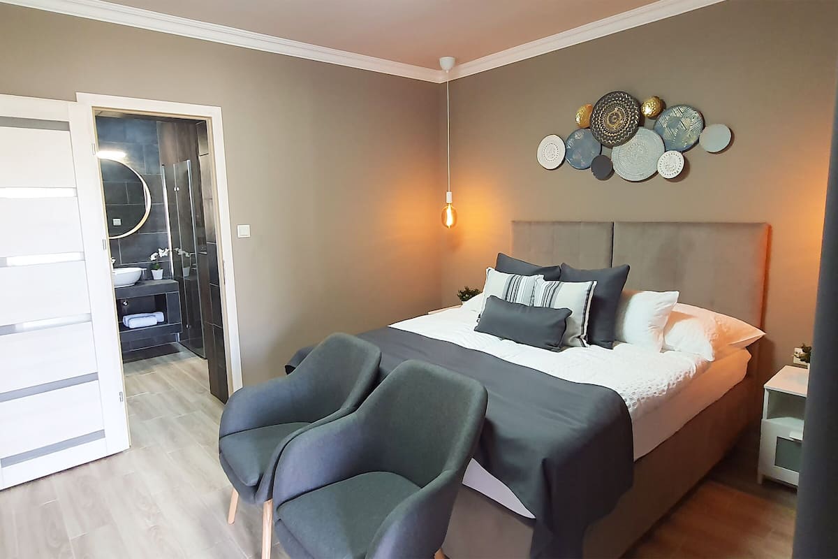 A bedroom with a bed, two chairs, a bedside table, and a wall decoration.