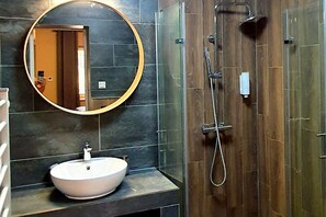 Bathroom features a round mirror, vessel sink, and glass-enclosed shower with handheld showerhead.