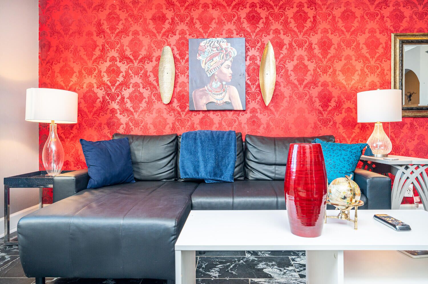 A modern living room with a red patterned wallpaper, a black leather sofa, and a white coffee table.