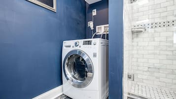 Pequeña lavandería con lavadora de carga frontal, zona de ducha con azulejos y pared azul.