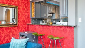 A compact kitchen with grey cabinets, a red patterned wall, and two green bar stools. - ATL Downtown Condo with Free Parking (Atlanta)