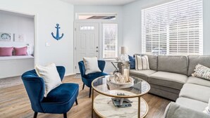 Una sala moderna con un sillón azul, una mesa de centro redonda y un sofá gris.