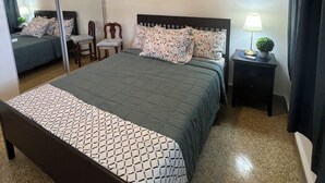 Un dormitori amb un llit, un ventilador de sostre, una tauleta de nit amb una làmpada i un mirall.