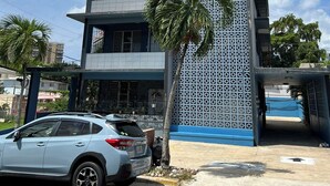 Un edifici de diversos pisos amb façana treballada, un cotxe estacionat i una palmera al davant.
