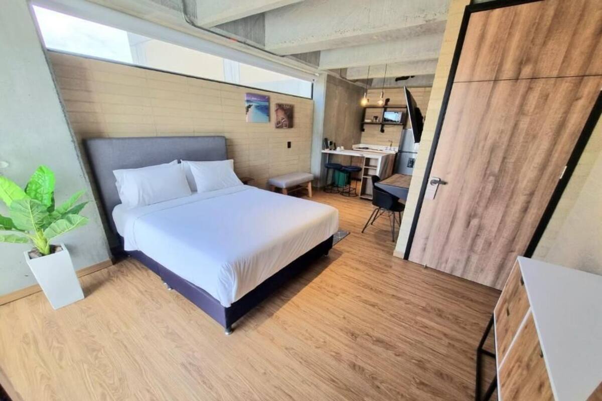 A modern bedroom with a large bed, a small desk, and a potted plant.