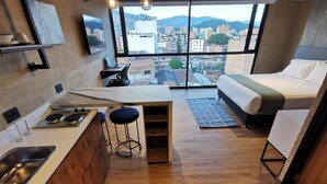 Una stanza compatta con angolo cottura, un letto e un'ampia finestra con vista sulla città.