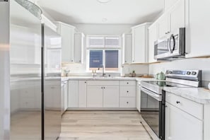 A modern kitchen with white cabinets, a stainless steel refrigerator, a microwave, and a built-in oven. - Beach Happy (Ocean Shores)
