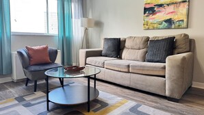 Ein modernes Wohnzimmer mit einem beigefarbenen Sofa, einem Glastisch und einem blauen Sessel.