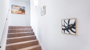 A staircase with beige carpeted steps leading upwards, flanked by white walls with three framed artworks. - La Vida Loca Stay in Baton Rouge near LSU - BC1011 (Baton Rouge)