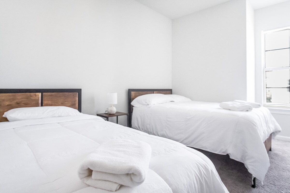 Una camera d'albergo con due letti, un comodino, una lampada e una finestra.