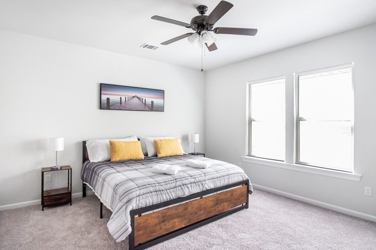 A bedroom with a bed, a ceiling fan, a nightstand, a lamp, and a window.