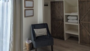 Une pièce avec un fauteuil sombre, une armoire en bois et une étagère blanche où sont pliées des serviettes.