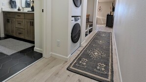 Un couloir avec un lave-linge, un évier avec un miroir et un tapis.