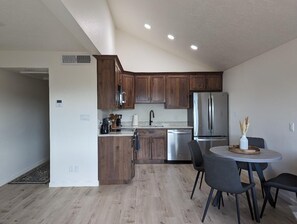 Eine moderne Küche mit Holzschränken, Edelstahlgeräten und einem Essbereich mit rundem Tisch und Stühlen.