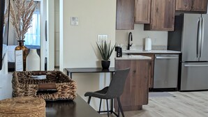 Une cuisine moderne avec des meubles en bois, un réfrigérateur en acier inoxydable et un petit îlot central agrémenté d’un tabouret.