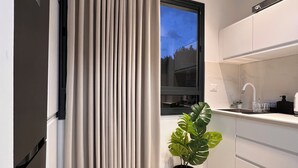 A modern kitchen with a window, a potted plant, and a curtain. - White Door Apartments (Haifa)