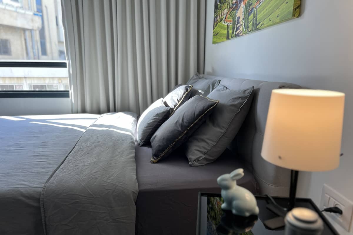 A modern hotel room with a neatly made bed, grey bedding, and a lamp on the side table.