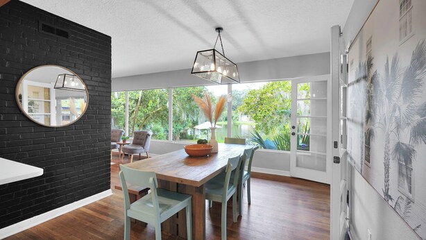 A modern dining area with a wooden table and chairs, a black brick accent wall, and a large window with a view of greenery.
