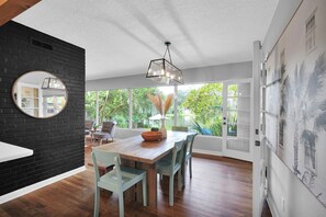 A modern dining area with a wooden table and chairs, a black brick accent wall, and a large window with a view of greenery.