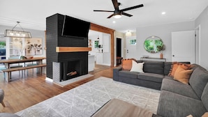 A modern living room with a fireplace, a ceiling fan, and a dining area with a bench.