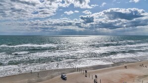 Una playa con olas, cielo despejado y algunas personas.
