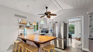 Une cuisine moderne dotée d’un îlot central, de tabourets de bar, d’un réfrigérateur en acier inoxydable et d’un ventilateur de plafond.