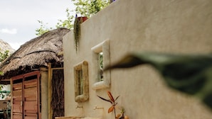 A rustic outdoor setting with a thatched-roof structure, a concrete wall, and a small table with a bowl and potted plants. - Aldea Toktli Hotel and Museum - Pool, Starlink Wi-Fi, and Mayan House Museum Tour (Izamal)