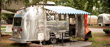 A vintage trailer with an open side, a table, and chairs set up for dining.