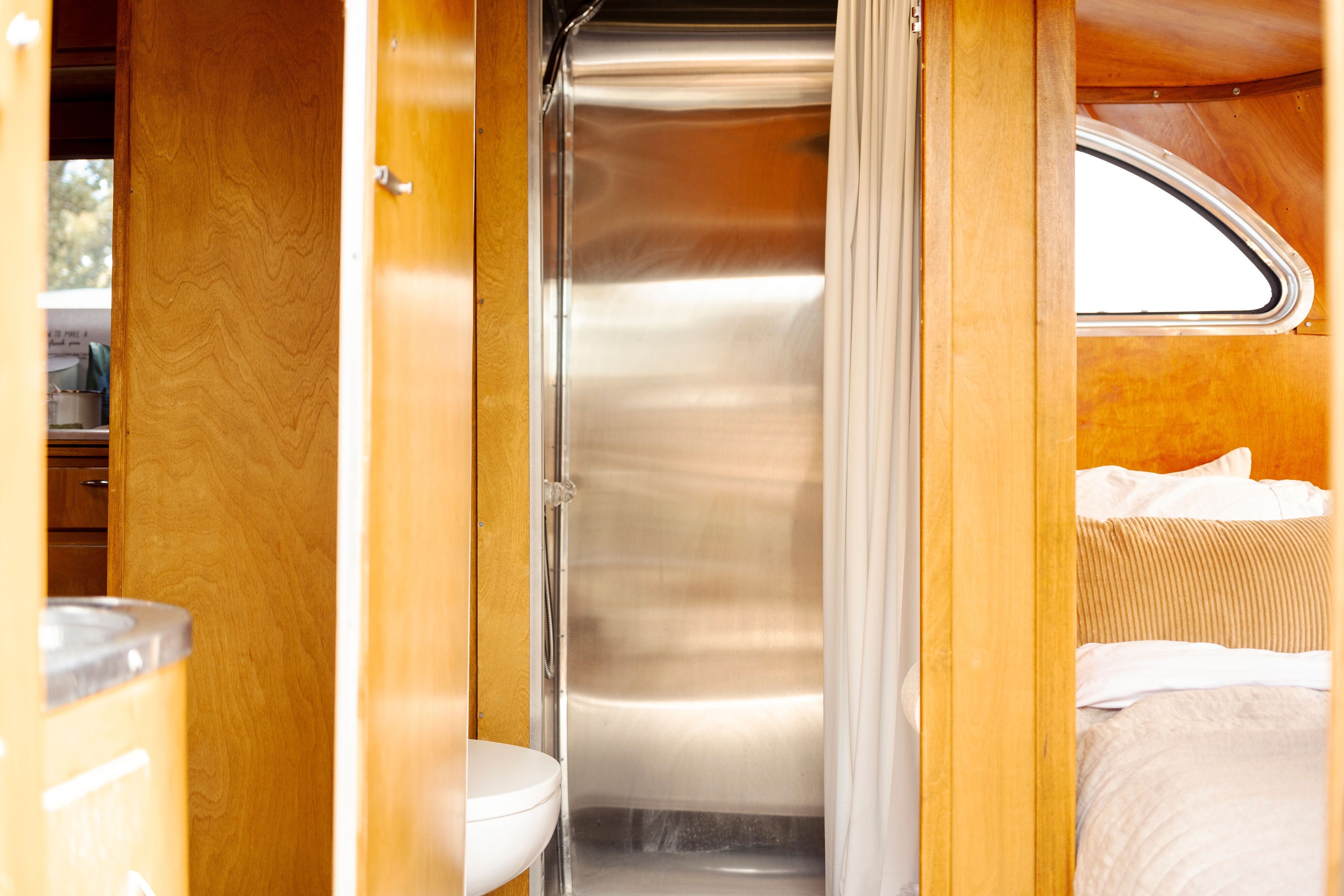 A compact bathroom with a toilet and shower area, wooden walls, and a window.